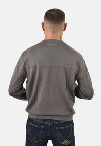 Maglione grigio con texture, collezione rotonda e dettagli sulla cucitura posteriore, abbinato a jeans blu scuro con accenti di cucitura a contrasto.