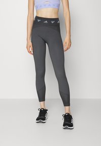 Gray textured leggings with a high waistband featuring a logo, paired with black running shoes and a light purple cropped top.