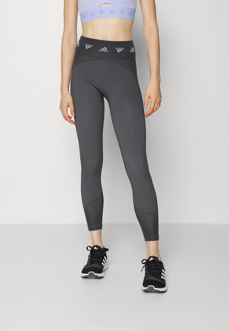 Gray textured leggings with a high waistband featuring a logo, paired with black running shoes and a light purple cropped top.