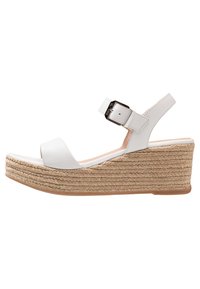 Valkoiset korkeat sandaalit, joissa on teksturoitu juuttikanta, säädettävä nilkkavarsi ja sileä varvasremmi. Kumipohja pitoa varten.