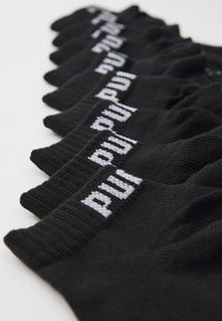 Calcetines negros hasta el tobillo dispuestos en una fila, con una textura acanalada y detalles de logotipo blanco en el borde superior. El material parece suave.