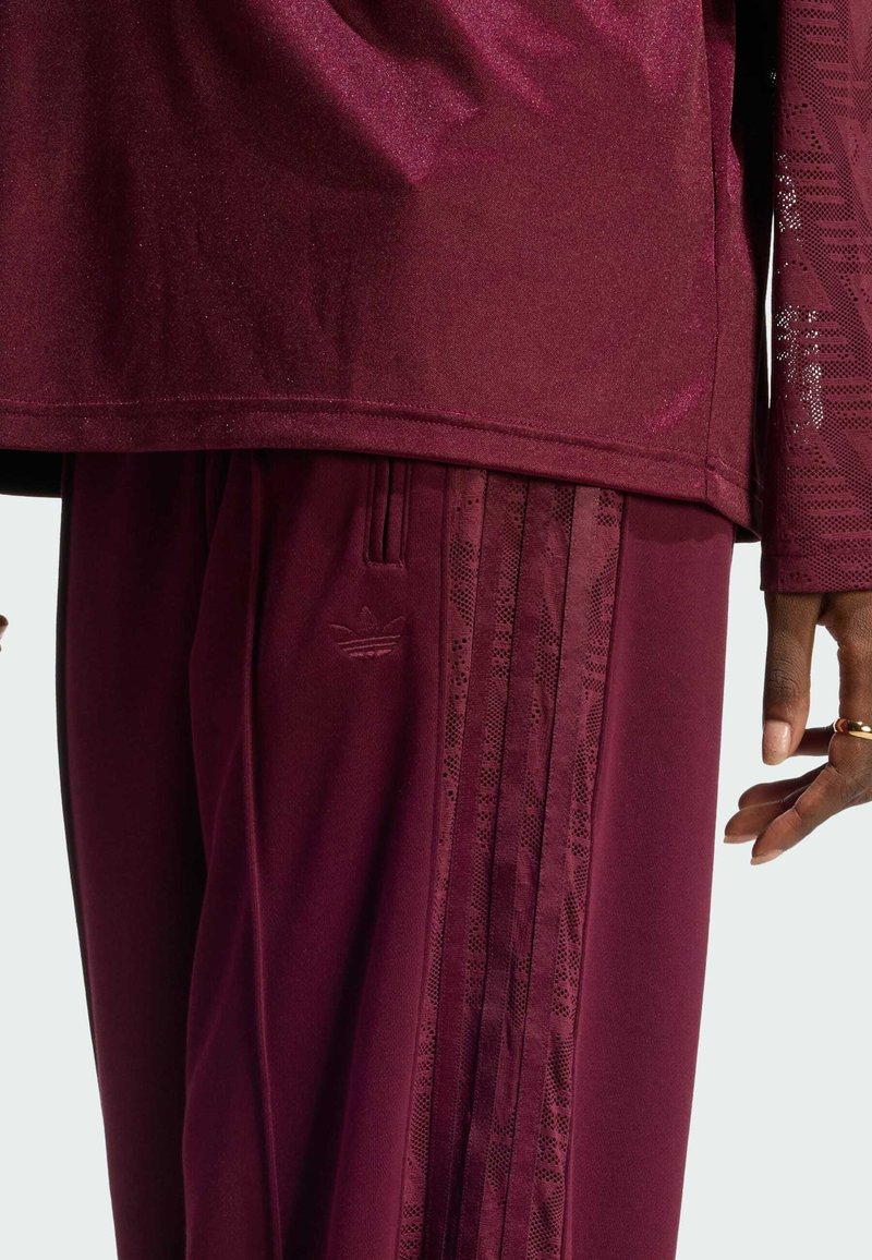 Survêtement athlétique bordeaux comprenant un haut texturé et un pantalon assorti avec trois bandes. Tissu lisse avec un léger éclat et détail de marque.