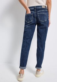 Jean en denim bleu foncé avec une coupe droite, ourlets retroussés et deux poches arrière. Une étiquette en cuir est visible au niveau de la taille.