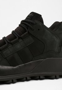 Svart Adidas-sneaker med tjock sula, mesh-tunga, ovandel i mocka och tre signaturstrimmor på sidan med svarta snören.