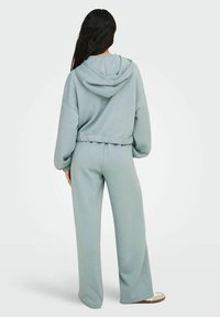 Lyseblå to-delt antrekk med en hettegensere i avslappet passform og matchende høytlivs, vide bukser. Myk tekstur.