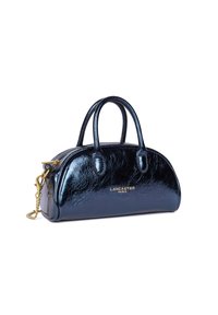 Sac à main noir, brillant, de forme arrondie, avec des anses doubles et une bandoulière en chaîne dorée. Présente un logo en relief doré à l'avant.