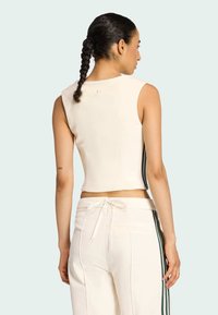 Krémový cropped top bez rukávov s okrúhlym výstrihom, krátkymi rukávmi a zelenými bočnými pruhmi; látka sa zdá byť hladká a priliehavá.