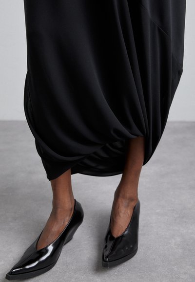 Black, flowing skirt with a gathered design at the hem, paired with shiny black wedge heels featuring a pointed toe and sleek finish.