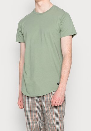 Zielona bawełniana koszulka z krótkim rękawem, okrągłym dekoltem i zaokrąglonym dołem, w zestawie z wielobarwnymi spodniami w kratkę z elastycznym pasem.