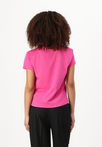 T-shirt aderente a maniche corte in cotone rosa brillante, con scollatura rotonda e una texture liscia, abbinato a pantaloni neri a righe verticali.