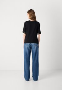 T-shirt noire à manches courtes, avec des finitions à motifs sur les poignets et le col ; associé à un jean en denim bleu ample.