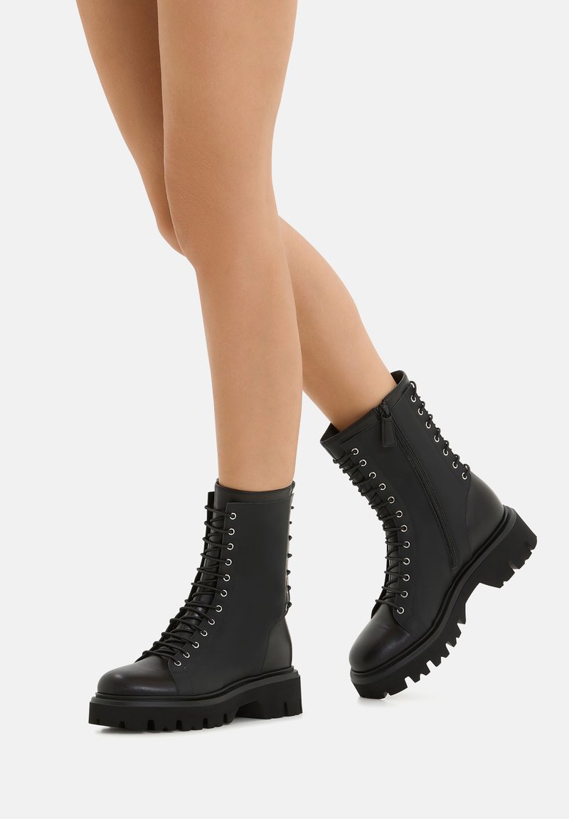 Stivali da combattimento in pelle nera con suola spessa, allacciatura frontale, occhielli in argento, cerniera laterale e dettagli rigati lungo il retro.