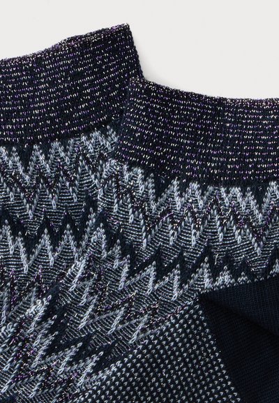 Gros plan sur un tissu tricoté bleu marine avec des motifs géométriques en zigzag et en losange en fils blancs et bleu clair.