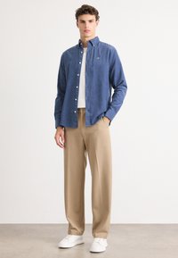 Een button-up overhemd van blauwe stof, beige wijde broek en witte sneakers. Glad textuur, casual ontwerp en contrasterende kleuren.