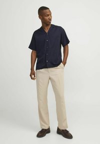 Short-sleeve navy shirt with a button-up design, paired with light beige trousers and dark brown shoes, set against a neutral background.