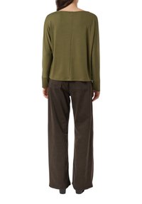 Sweter oliwkowej zieleni z szerokim dekoltem i długimi rękawami, połączony z luźnymi, ciemnobrązowymi spodniami. Prosty design, miękka faktura.