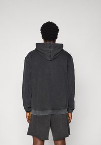 Schwarzer Hoodie mit Kordelzugkapuze, lässiger Schnitt, gerippte Bündchen und Saum. Trägt dazu passende schwarze Shorts aus strukturiertem Stoff, minimalistisches Design.