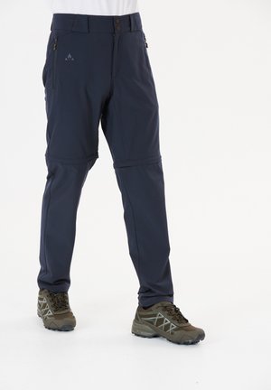 Marinefarbene Outdoor-Hosen mit schmalem Schnitt, zwei Reißverschlusstaschen und glatter Textur, kombiniert mit braunen Wanderschuhen mit grauen Akzenten.