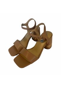 Sandali con tacco a blocco in pelle color pelle, con punta quadrata e cinturino alla caviglia. Presentano una finitura lucida e un accento dorato sul tacco.