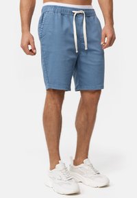 Lyseblå shorts med snøre i taljen, sidelommer og lukkede kanter. Båret med hvide sneakers med struktureret overdel og tyk sål.
