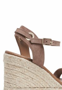 Sandalia de cuña de ante marrón con tacón de yute trenzado, que presenta un diseño de doble tira y un sencillo detalle de hebilla metálica.
