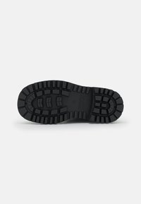Suela de bota de goma negra con un patrón de relieve resistente, características de ranuras profundas y lugs de amortiguación para tracción y durabilidad.