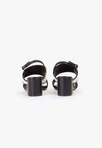Sandali neri con tacco a blocco, caratterizzati da un design a cinturino incrociato. Realizzati in pelle, con cinturini alla caviglia regolabili e una texture liscia.