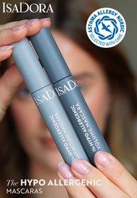 Due tubetti di mascara grigi etichettati "Definizione" e "Volume" tenuti in una mano, con un badge di certificazione per allergie nell'angolo.