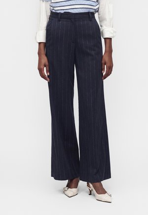 Pantaloni a righe sottili blu navy scuro a gamba larga indossati con tacchi slingback bianchi appuntiti e top a righe con maniche risvoltate.