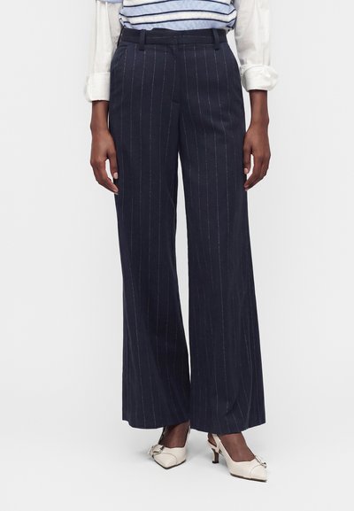 Pantalon large à fines rayures bleu marine foncé porté avec des escarpins slingback blancs pointus et un haut rayé à manches retroussées.