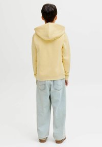 Sweat-shirt à capuche jaune avec une coupe décontractée, associé à un jean ample bleu clair. Texture de tissu lisse, design minimaliste, détails de couture simples.