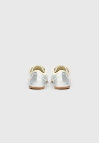 Sapatilhas de balé prateadas com biqueira arredondada, material superior macio e sola de borracha castanha. Apresentam um calcanhar em creme contrastante e detalhes elásticos nas laterais.