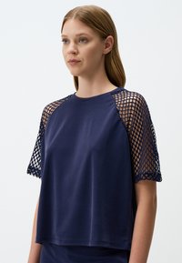 Top blu navy con maniche corte a rete. Tessuto morbido con un taglio rilassato, scollatura rotonda e design intricato delle maniche.