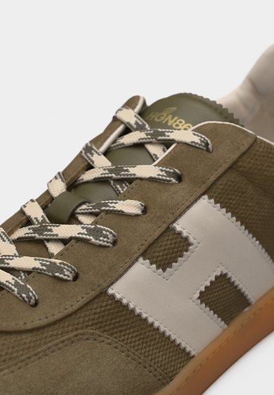 Baskets vertes et beiges avec lacets à motifs, logo latéral "H" blanc, et semelle en gomme, gros plan sur l'avant supérieur et la zone de laçage.