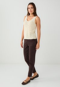 Jasbeżowy dzianinowy top na ramiączkach z dekoltem w serek, zestawiony z ciemnoniebieskimi dopasowanymi spodniami. Modelka nosi czarne perforowane baleriny. Minimalistyczne dodatki.