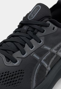 Black athletic shoe featuring a breathable mesh upper, textured overlays, gray accents, and a durable rubber sole with laces.