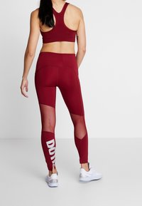 Reggiseno sportivo bordeaux e leggings con pannelli in rete e lettering bianco. I leggings presentano una vestibilità aderente e un tessuto testurizzato. Scarpe da ginnastica bianche.