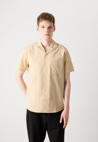 Kurzärmliges, knöpfbares Hemd aus hellgelbem Textil mit einer Brusttasche und einem lässigen Kragen, kombiniert mit schwarzen Hosen.