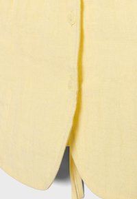 Gros plan sur un tissu jaune clair avec deux petits boutons translucides cousus sur une couture verticale.