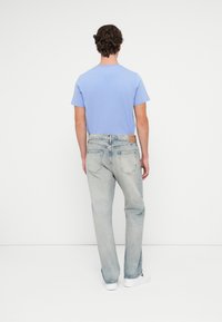 Svetlomodré tričko s krátkymi rukávmi, skombinované s bledomodrými džínsami a bielymi teniskami. Viditeľný kožený štítok na páse.