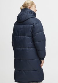 Navy blue puffer coat with a hood, featuring a quilted design, voluminous shape, and elastic cuffs for warmth and comfort.