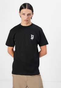 Sort bomulds t-shirt med et lille hvidt grafisk logo på venstre bryst. Klassisk Crew neck og korte ærmer, med en afslappet pasform.