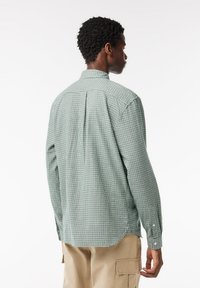 Camicia verde a quadri con maniche lunghe, colletto button-down, dettagli di pieghe sul retro e vestibilità rilassata. Tessuto di cotone liscio con una leggera texture.