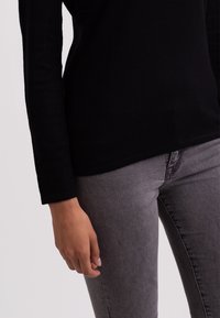 Svart långärmad topp som kombineras med grå tajta jeans. Tyget verkar slätt, med en rakt ribbad struktur på ärmarna och rena fållar.