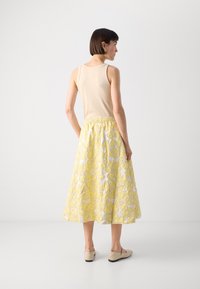 Un débardeur beige associé à une jupe fleurie jaune avec une broderie texturée et une ceinture élastique, complété par des chaussures slip-on beiges.