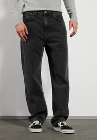 Svart denimjeans med avslappet passform, med frontlommer og knappelukking. Kombinert med svart og hvit lerrets sneakers.