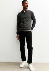 Dunkelgraues langärmeliges Polohemd mit Reißverschluss, kombiniert mit schwarzen Slim-Fit-Hosen und weißen Sneakers vor einem hellen Hintergrund.