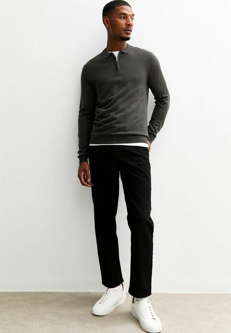 Dunkelgraues langärmeliges Polohemd mit Reißverschluss, kombiniert mit schwarzen Slim-Fit-Hosen und weißen Sneakers vor einem hellen Hintergrund.