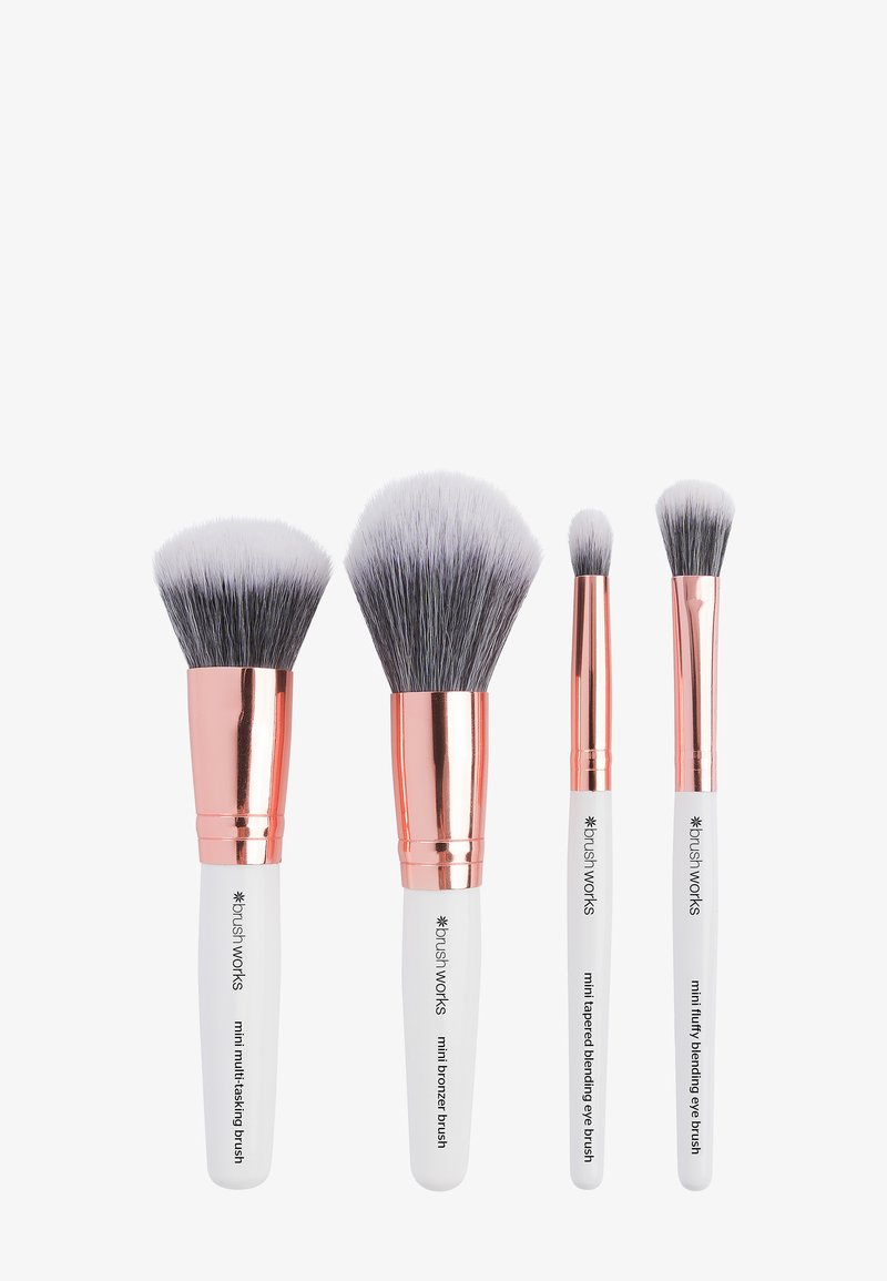 Quattro pennelli per il trucco con manici bianchi e ferrule in oro rosa, di dimensioni e forme diverse per l'applicazione su viso e occhi.
