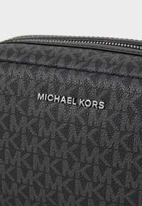 Schwarze, strukturierte Tasche mit einem Monogramm-Muster, silberner Hardware und einem auffälligen "MICHAEL KORS"-Logo auf der Vorderseite.